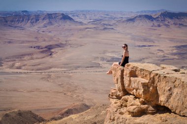 Uçurumda oturan bir kız çöl Negev manzarasına bakıyor. İsrail 'de yaz tatili