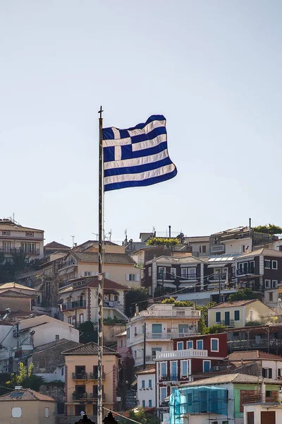 Grekisk flagga vinkar vid solnedgången. Hus på bakgrunden. — Stockfoto
