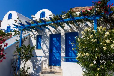 Yunanistan 'ın Santorini adasında mavi kapısı ve çiçek açan begonvil bitkisi olan Yunan beyaz evi