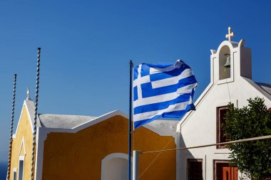 Mavi gökyüzüne ve Yunan mimarisine karşı dalgalanan Yunan bayrağı