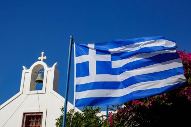 Mavi gökyüzüne ve Yunan mimarisine karşı dalgalanan Yunan bayrağı