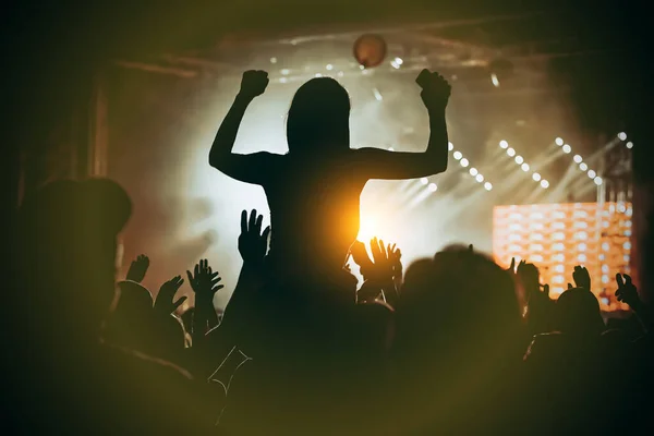 Girl silhouette with raising hands and mobile phone during enjoying music concert
