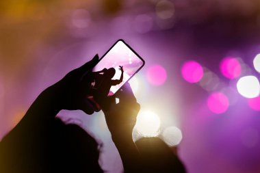 Müzik bandosu hayranı bir konseri fotoğraflamak için akıllı telefonu tutuyor.