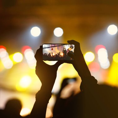 Müzik bandosu hayranı bir konseri fotoğraflamak için akıllı telefonu tutuyor.