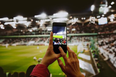 Akıllı telefondan futbol maçının fotoğrafını çeken bir hayran. Stadyumdaki cep telefonu kamerasını kullanarak.