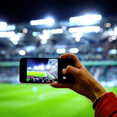 Stadyumdaki bir futbol maçının fotoğrafını çekmek için akıllı telefon kamerası kullanmak..