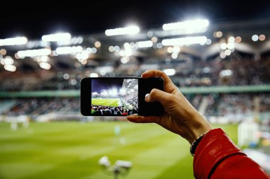 Akıllı telefondan futbol maçının fotoğrafını çeken bir hayran. Stadyumdaki cep telefonu kamerasını kullanarak.