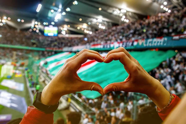 She loves this team. Heart shape for the favorite football club during a match in a stadium.