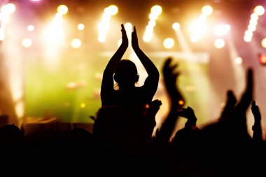 Rock konserindeki kız silueti parlak sahne ışıkları önünde. Yaz müzik festivalinde zevk