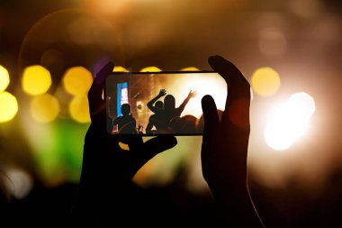 Cep telefonlu bir konser kaydı, akıllı telefonlu eller silueti.