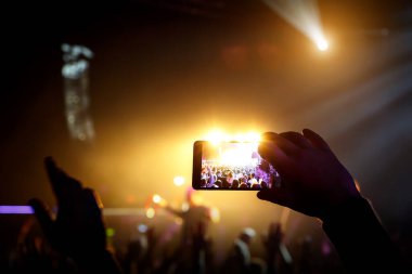 Canlı konserde akıllı telefonu ve sahnede ışıkları alan bir adam..