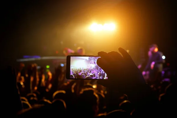 Man taking smart phone at live concert and lights on stage.