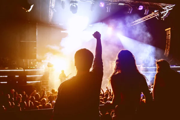 Back view of girl with hands up standing in stage lights.