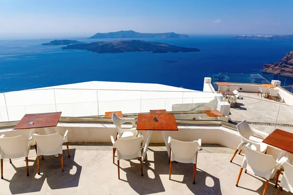 Santorini 'de güneşli bir terasta boş restoran masaları. Arka planda deniz ve kaldera