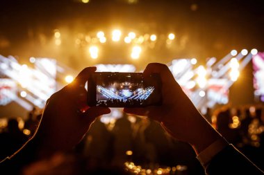 Fan akıllı cep telefonunu tutuyor ve bir rock konserinin fotoğrafını çekiyor.