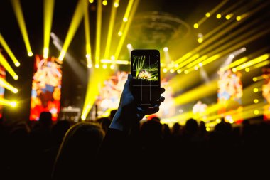 Fan akıllı cep telefonunu tutuyor ve bir rock konserinin fotoğrafını çekiyor.