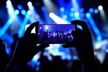Bir müzik konserinin fotoğraflarını çekmek için ellerinde akıllı telefon.