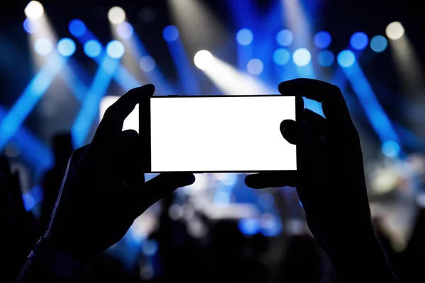 Smartphone in a hands on a music concert show, blank white screen mockup