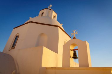 Turuncu günbatımında Santorini adasındaki beyaz kilisenin çan kulesi.