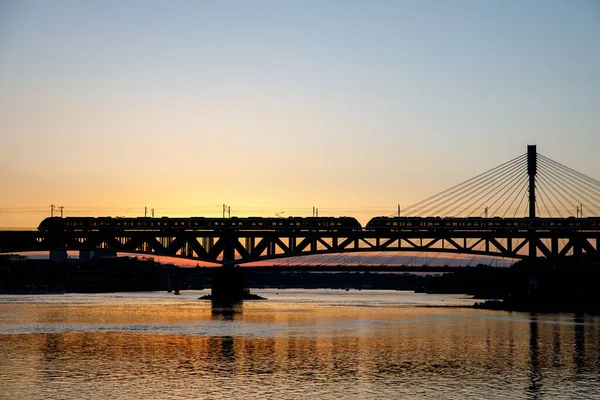 電車は日没時に川の上のケーブルカーに乗って橋を渡った — ストック写真