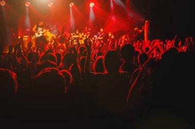 A crowd of happy people raising up hands at an open-air rock concert