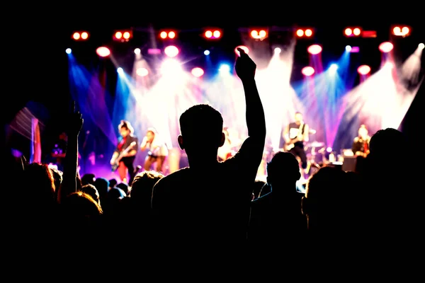 A crowd of happy people raising up hands at an open-air rock concert