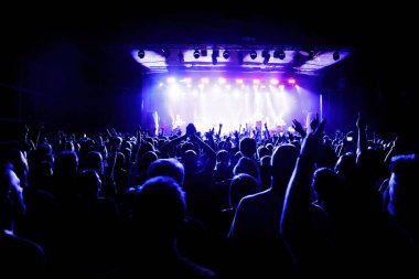 A crowd of happy people raising up hands at an open-air rock concert