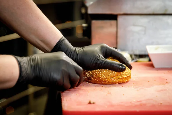 The process of making a burger in a restaurant kitchen. The chef in black gloves cut the bun