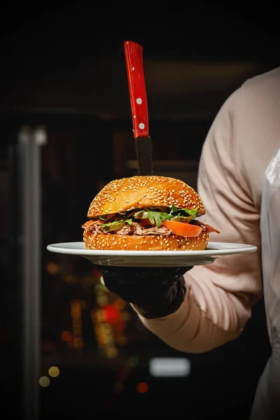 The chef of the restaurant holding a cooked burger in the hands