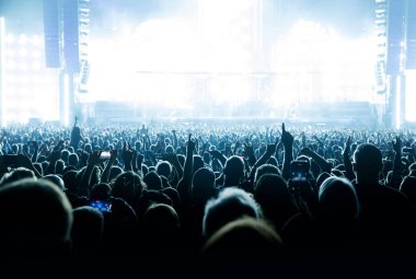 Silhouettes of people with raised hands against the stage light. Cheering crowd on the music show