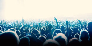 Silhouettes of people with raised hands against the stage light. Cheering crowd on the music show