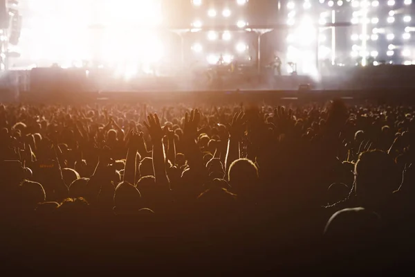 Performance of a popular group. The crowd with raised hands against the stage light