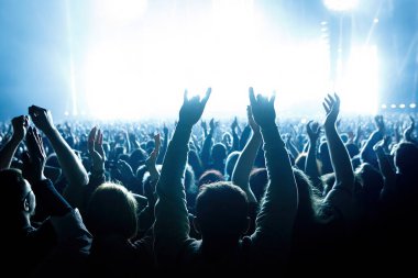 Performance of a popular group. The crowd with raised hands against the stage light