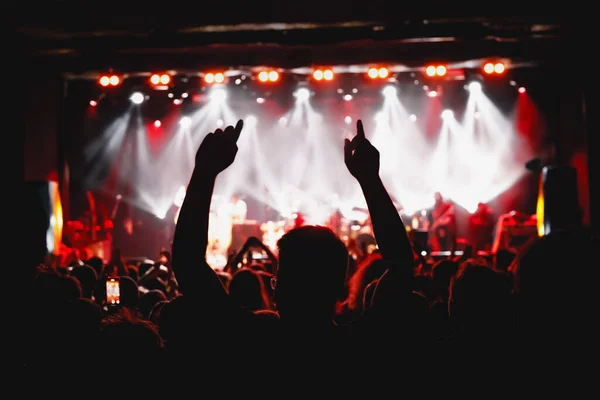 The man with raised hands during the music concert. Crowd and stage light in a concert hall