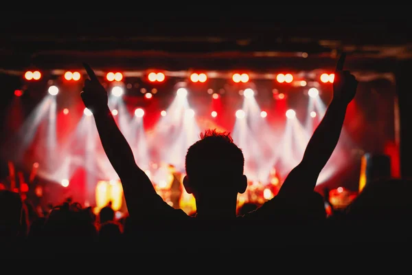 The man with raised hands during the music concert. Crowd and stage light in a concert hall