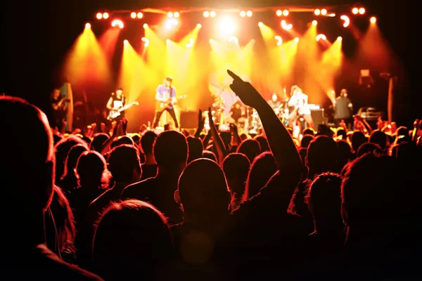 The man with raised hands during the music concert. Crowd and stage light in a concert hall