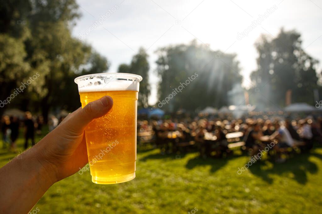 A plastic glass of beer in hand. Outdoor summer festival
