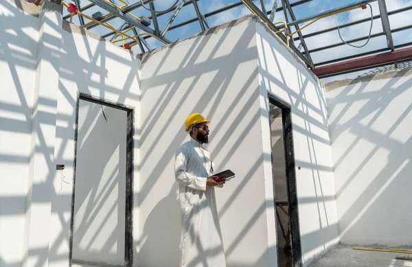 Geleneksel üniforma ve güvenlik kaskı giymiş Orta Doğu Arap mühendisleri konut alanlarındaki inşaat projelerini denetliyorlar.