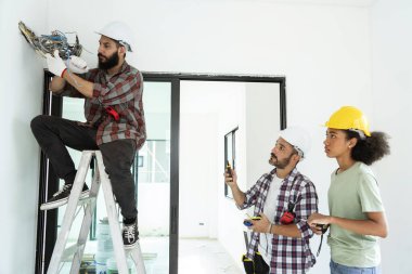 Elektrik müteahhiti elektrik dolaplarını incelemek ve onarmak için merdivenleri çıkmış. Foreman ekibi de inşaatı bir kadın işçinin inşaatta durduğu kadar doğru şekilde incelemiş.. 