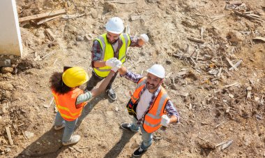 Mühendisler ve iş arkadaşları güvenlik üniforması giyer ve mühendis miğferleri konut projesinde çalışanlarla el ele tutuşur. Takım çalışması ve başarı konsepti.