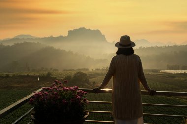 Tatillerde seyahat ederken dinlenmek için şapka takan Asyalı kadınlar gün doğumunda dağların manzarasına hayran kalırlar. 