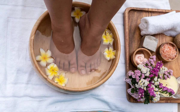 Foot spa  ,wellness and Relax concept The masseur washes his bare feet in a wooden tub with frangipani flowers and salt scrub and soap near swimming pool at the resort and spa .