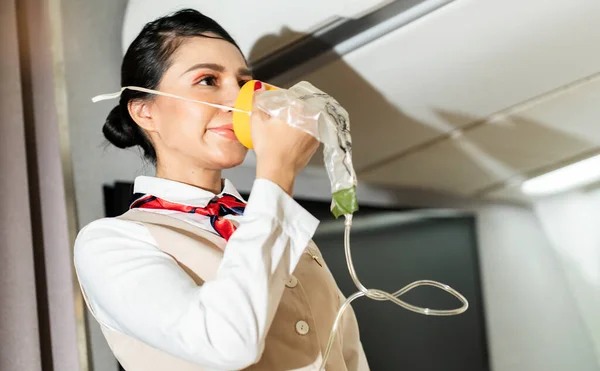 female flight attendant wearing a breathing apparatus demonstrates safety gear in the cabin before takeoff.Airline Service and traveler Concept