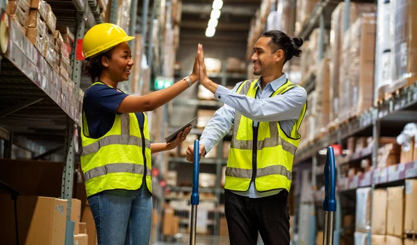 Uniformed African female worker wearing a Hi-Five engineer\'s hat and colleagues greet each other in a warehouse.Teamwork concept.