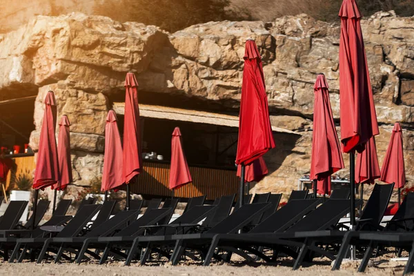 black sun loungers on the beach with red sun umbrellas. closed beach recreation complex on the seashore.