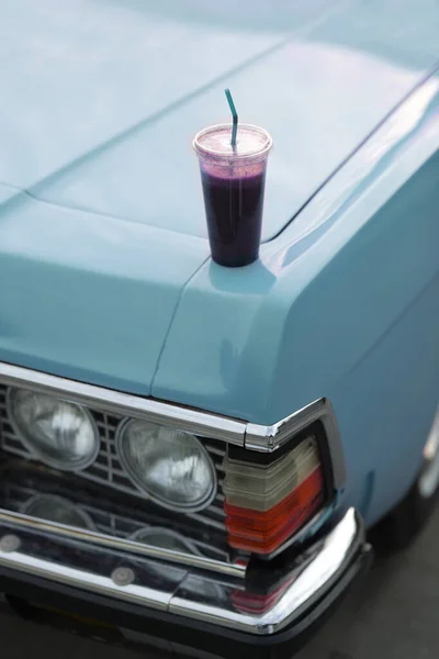 glass with a drink on the hood of a blue retro car close-up. coffee to go by car. headlight