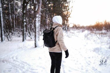 Bir adam kış ormanında tek başına yürür. Sırt çantalı bir turist, karla kaplı kozalaklı ormanda yürüyor.