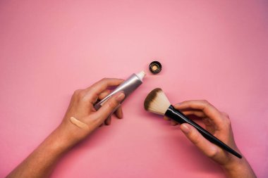 Pembe arka plan manzaralı bir fırçayla yüzün temelini tutan eller. Makyaj malzemeleri. Yüz için dekoratif komedi. yüz bakımı ürünü. temel modelleme