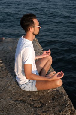 Spor giyimli bir gencin portresi gün doğumunda deniz kenarındaki bir rıhtımda meditasyon yapıyor. Sporcu adam okyanus tarafından meditasyona tabi tutulur.