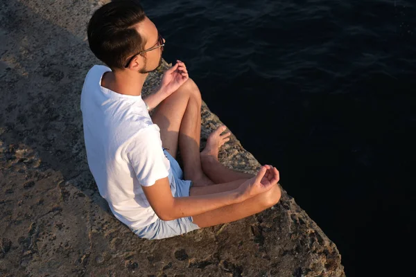 Spor giyimli bir gencin portresi gün doğumunda deniz kenarındaki bir rıhtımda meditasyon yapıyor. Sporcu adam okyanus tarafından meditasyona tabi tutulur.